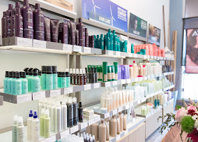 Shelves in a store display a variety of hair care products in bottles and tubes, organized by color and brand. - Gila Rut Salon | San Diego and Chula Visa, CA
